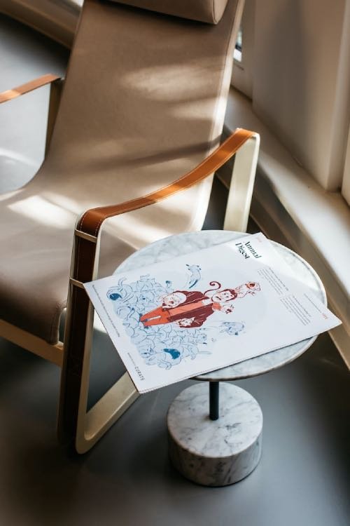 A magazine featuring an illustrated cover placed on a marble side table next to a chair.